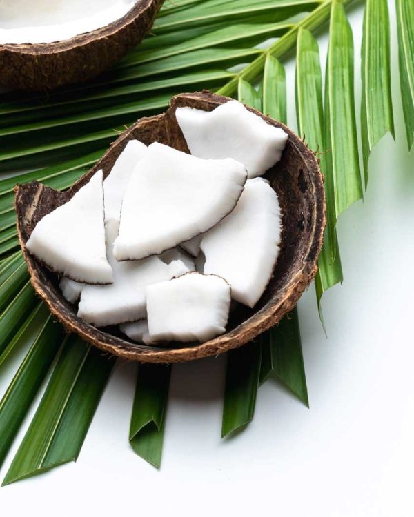 Coconut meat and coconut oil in glass bottle on coconut leaf.